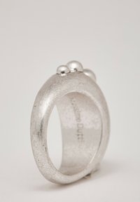 Anello d'argento con una fascia liscia e texturizzata e tre piccoli accenti sferici sulla parte superiore. Interno inciso con il nome del marchio.