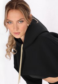 Indumento nero con cappuccio, dotato di un ampio colletto e cordoncino dorato. Tessuto liscio con una vestibilità morbida e un design corto.