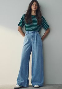 Camiseta de rayas verdes combinada con unos jeans de tiro alto y pernera ancha de color azul claro. El conjunto tiene un corte holgado y una textura de mezclilla clásica.