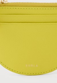 Porte-cartes en cuir vert citron avec fermeture éclair et trois emplacements pour cartes, embossé du nom de la marque "Furla" en petites lettres dorées.
