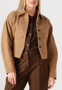 Bruine cropped jas van gestructureerde stof, met een kraag, knopen aan de voorkant en brede mouwen, gecombineerd met een bijpassende top en broek.