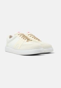 White sneakers made of suede and fabric, featuring a textured upper, beige laces, and a white rubber sole with minimal detailing.