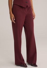 Burgundské kalhoty s širokými nohavicemi vyrobené z hladké látky, s plochým předním dílem, záhyby a upraveným střihem. Stylizované s botami s špičatou špičkou.