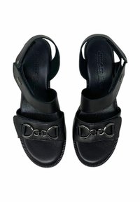 Sandali neri con finitura in pelle liscia, cinturini regolabili e dettaglio con fibbia metallica. Suole piatte con bordi testurizzati.