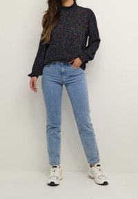 Blouse bleu marine à motif cachemire, col à volants et manches longues, associée à un jean droit bleu clair et des baskets blanches.