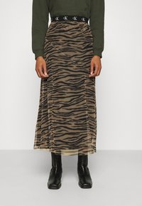 Genomskinlig maxikjol med tigertryck i beige och svart. Elastisk midja och en flytande, lätt textur. Svarta ankelstövlar på.