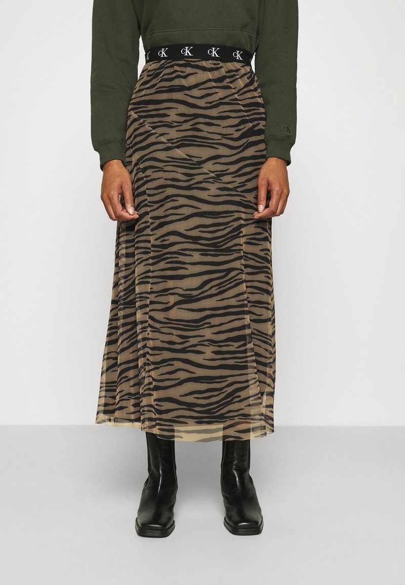 Genomskinlig maxikjol med tigertryck i beige och svart. Elastisk midja och en flytande, lätt textur. Svarta ankelstövlar på.