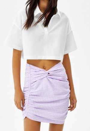 Witte cropped shirt met korte mouwen en een V-hals, gecombineerd met een lavendel kleurige ruitenrok met plooien en een gedraaide detail bij de taille.