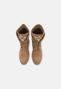 Botas de tobillo de ante marrón con cordones, que presentan adornos decorativos en el puño y una superficie lisa y texturizada.