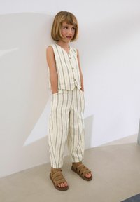 Tvådelad outfit med en ärmlös randig topp och lösa byxor i krämfärg med marinblå ränder. Kombinerad med bruna sandaler med spänne.