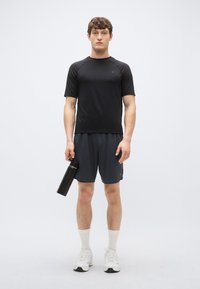 Svart kortärmad träningsskjorta och mörkgrå shorts, håller en svart vattenflaska. Vita sneakers med vita ankelstrumpor. Ren, minimalistisk design.