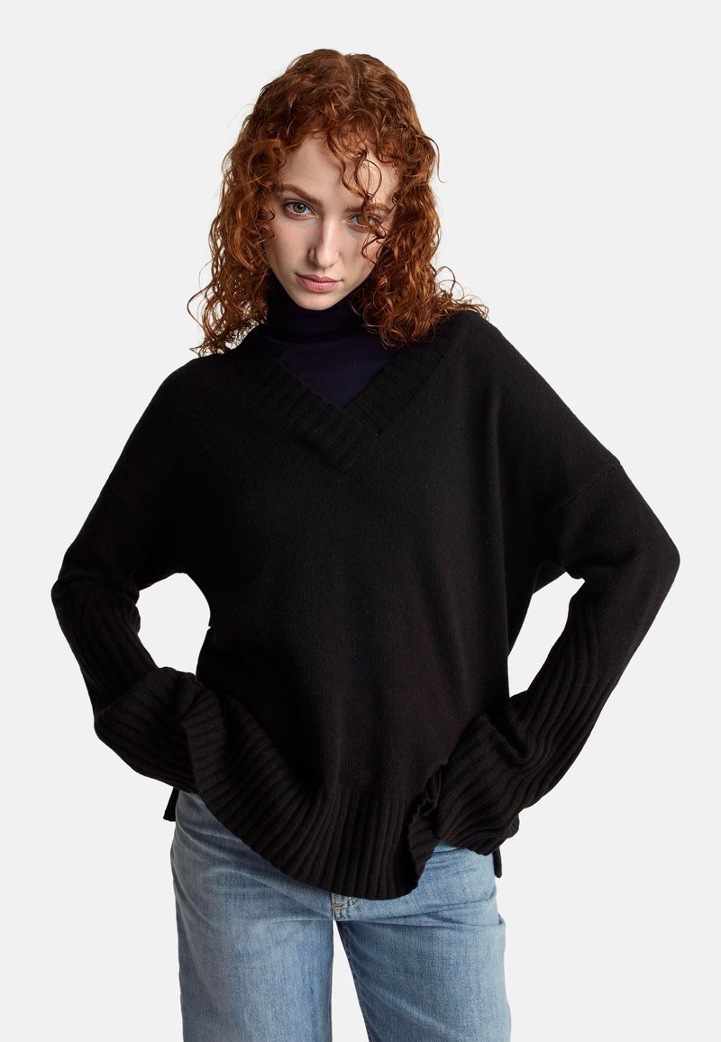 Czarny sweter z dzianiny z dekoltem w serek, ściągaczami przy mankietach i u dołu, luźny krój, zestawiony z jasnoniebieskimi dżinsami. Teksturowana, miękka tkanina.