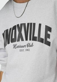 Felpa grigia con "KNOXVILLE" in bold lettering nero, caratterizzata da una scritta "Leisure Club" sotto e "EST. 1982." Tessuto testurizzato.