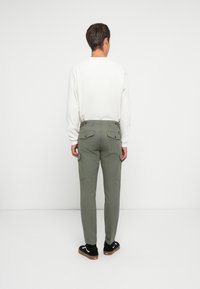Pantalons cargo légers de couleur vert olive avec deux poches arrière, coupe droite, et une chemise à manches longues texturée blanche. Baskets noires avec semelles en caoutchouc.