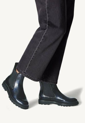 Botines de cuero negro con un acabado brillante, que cuentan con paneles laterales elásticos y suelas de goma resistentes, combinados con pantalones de corte ancho oscuros.