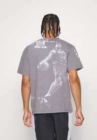 Grå bomulds T-shirt med et stort hvidt grafisk motiv af en basketballspiller på ryggen, rund halsudskæring og korte ærmer.