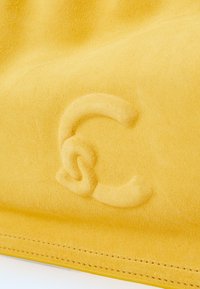 Un matériau en daim jaune présentant un logo en relief subtil. La surface a une texture douce, avec une finition lisse et des détails de couture soignés.
