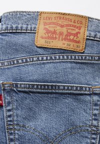 Jean Levi's bleu avec poche arrière visible et patch en cuir beige affichant le nom de la marque, le logo et la taille W32 L32.