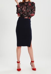 Blusa nera a fiori con maniche lunghe, abbinata a una gonna a tubino blu navy con uno spacco laterale. Completata con sandali con tacco alto rossi.