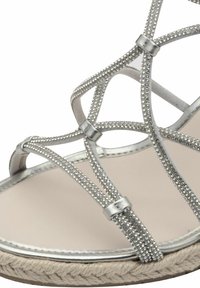 Stříbrné sandály na řemínky s třpytivými rhinestonovými kamínky, měkkou béžovou stélkou a tkanou podešví připomínající jutový materiál. Elegantní design s křížením.