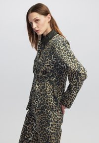 Set giacca e pantaloni con stampa leopardata in beige e nero, caratterizzato da un colletto in pelle, numerose tasche e un design strutturato.