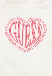 Cream hoodie featuring large red embroidered "GUESS" logo in a heart shape, with "CALIFORNIA" and "LOS ANGELES" text accentuating the design.