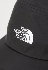 Zwarte stoffen bucket hat met een witte "The North Face" logo op de voorkant. Soepele textuur met een gestructureerde rand.