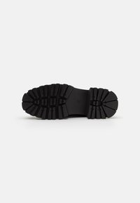 Black rubber shoe sole with deep traction grooves, rounded heel, and flat design. Textures create a durable and stable surface.
