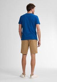 Blå bomulds T-shirt med rund udskæring, parret med lysbrune bomulds shorts. Hvide sneakers med beige accenter. Minimalistisk design, uden mønstre.