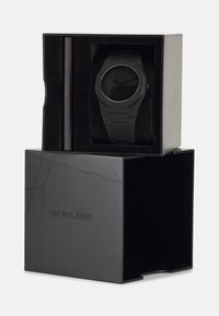 Svart analog klokke med rund skive og teksturert reim, vist i en svart boks med "D1 MILANO"-logoen preget på siden.