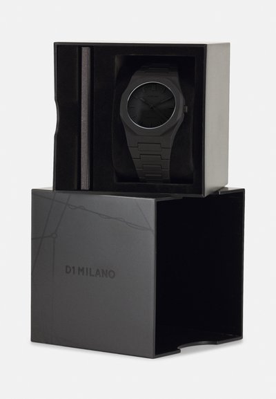 Zwarte analoge horloge met een ronde wijzerplaat en een geborsteld bandje, tentoongesteld in een zwarte doos met het "D1 MILANO" logo erin gedrukt aan de zijkant.