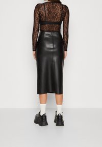 Schwarzer Leder-Midi-Rock mit glatter Textur, kombiniert mit einem transparenten, schwarzen Spitzenoberteil mit langen Ärmeln. Schuhwerk: klobige schwarze Sneakers, weiße Socken.