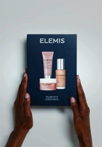 Set regalo di prodotti skincare Elemis in una scatola blu scuro con un tubo di crema rosa, un barattolo bianco e una bottiglia di vetro. Scatola etichettata "PLUMP IT UP."