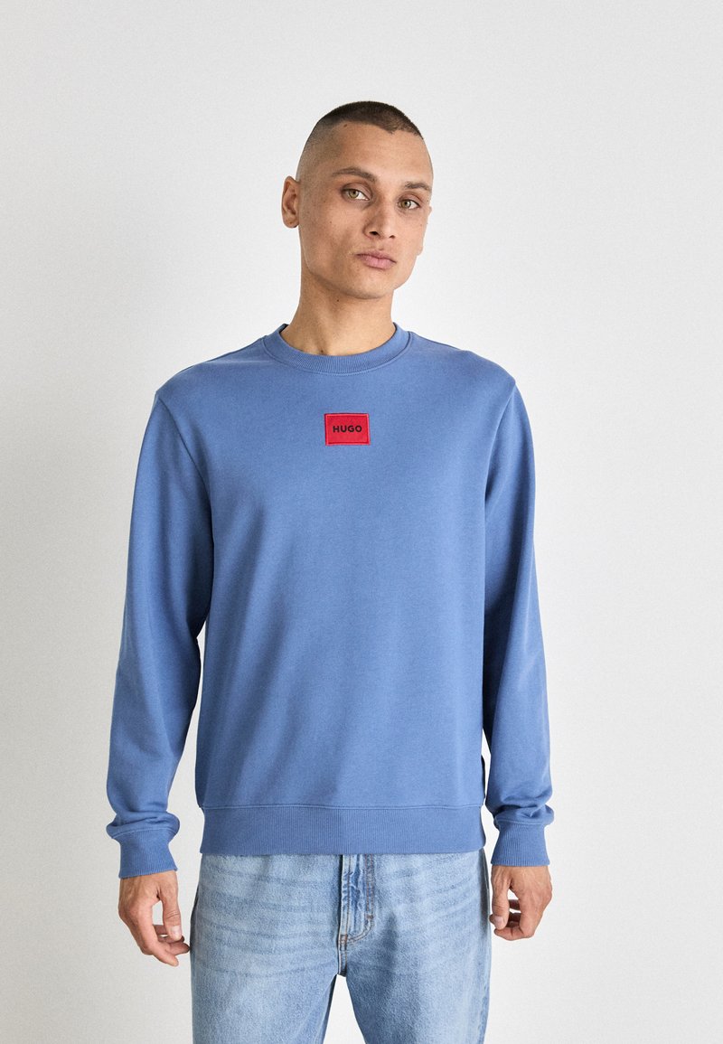 Felpa azzurra chiara con maniche lunghe e collo rotondo. Presenta una tasca logo rettangolare rossa sul petto. Tessuto morbido, vestibilità casual.