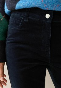 Marineblå corduroy bukser med en glat tekstur, der har frontlommer og et sølvfarvet knaplukning i taljen.