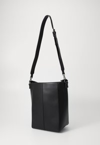 Svart faux läder tote-väska med rektangulär form, justerbar rem, slät textur och minimalistisk design, med en central sömdetalj.