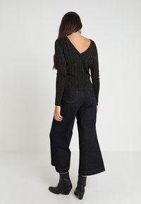 Svart, texturerad långärmad topp med V-raglan-design, parat med högmidjade mörka denimbyxor med vida ben och klumpiga svarta ankelskot.