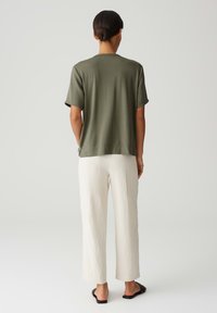 Top verde oliva a maniche corte con una vestibilità rilassata, abbinato a pantaloni a gamba larga color avorio, caratterizzati da una texture leggera e un design semplice.