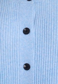Svetlo modra rebrasta jopica s črnimi gumbi, s poudarkom na vertikalni teksturi in gladkem zaključku. Vidni šivi vzdolž gumbevega roba.