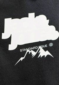 Sudadera negra con texto gráfico blanco "jack & jones" y "STANDARD ISSUE" sobre un diseño estilizado de montaña. Material de algodón, corte casual.