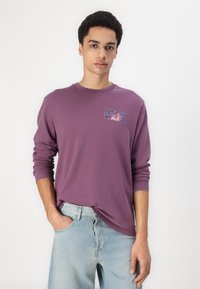 Purple long-sleeve t-shirt with "STAR WARS" graphic on the chest, made from cotton fabric, paired with light blue jeans.