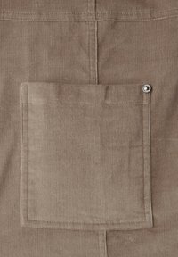 Brun manchester tyg med en enda fyrkantig ficka med metallknapp. Texturen visar tydliga räfflor som är typiska för manchester.