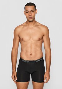 Fekete boxer alsónadrág sima textúrával, fehér logós elasztikus derékkal. A design testhez simuló, amely hangsúlyozza az áramvonalas sziluettet.