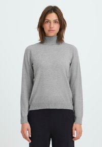 Grauer Rollkragenpullover aus weichem Strickmaterial, mit langen Ärmeln und gerippten Säumen, kombiniert mit dunklen Hosen.