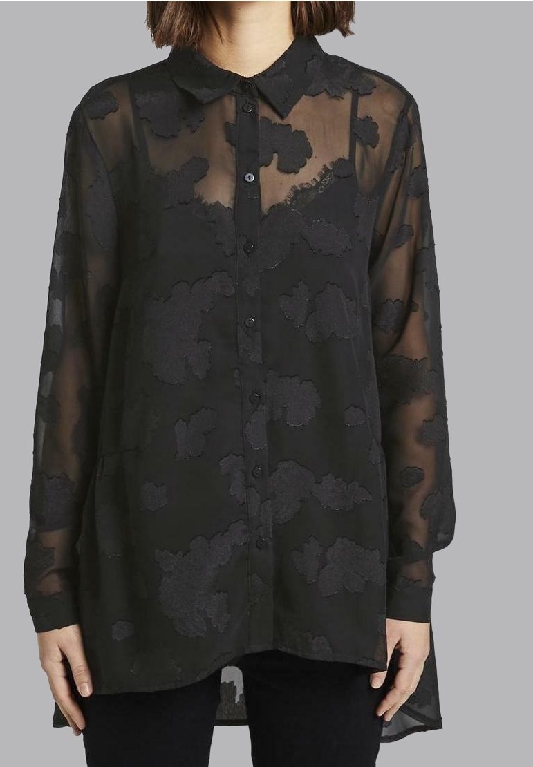 Blouse noire transparente avec fermeture boutonnée sur le devant, manches longues, col pointu et motif floral texturé. Ourlet arrondi et coupe décontractée.