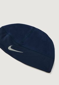 Sötétkék sportsapka rugalmas anyagból, matt felülettel és fényvisszaverő ezüst Nike logóval az oldalán.