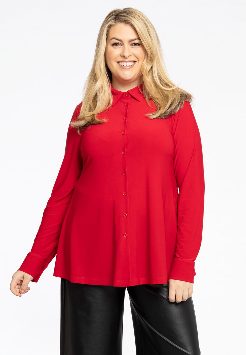 Chemise rouge à manches longues avec col, présentant une coupe ample et une texture lisse, associée à un pantalon en cuir noir.