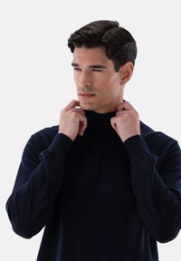 Marineblaue Rollkragenpullover aus einem weichen, strukturierten Strick. Mit langen Ärmeln und figurbetontem Design, das am Kragen gerafft ist.