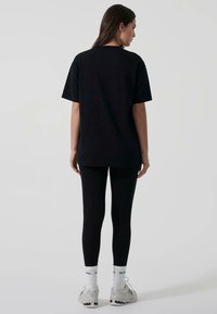 Svart oversized t-shirt med korta ärmar, parat med svarta leggings. Bärs med vita strumpor och sneakers med en strukturerad sula.