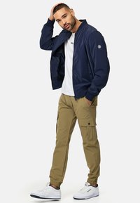 Marine bomberjakke, hvid t-shirt, beige cargo bukser og hvide sneakers. Jakken har ribbede manchetter og lynlås-lukning. Cargo bukserne har sidelommer.